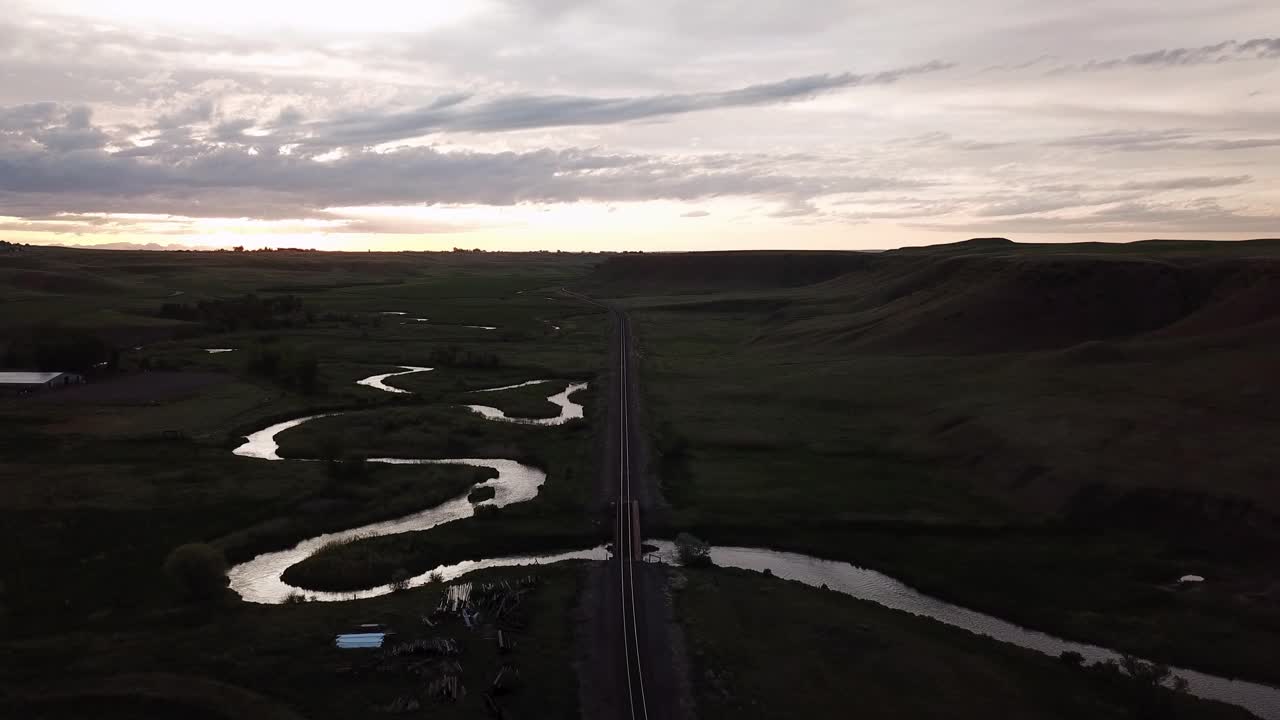 航拍的铁路轨道在蜿蜒的河流对着天空，无人机在黄昏飞行向前景观-比林斯，蒙大拿州视频素材