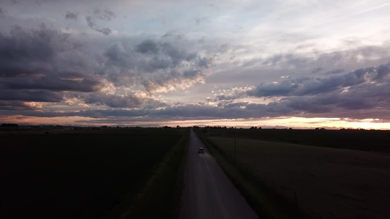 在多云的天空下，汽车行驶在植物之间的道路上，无人机在黄昏时向前飞行，蒙大拿比林斯视频素材