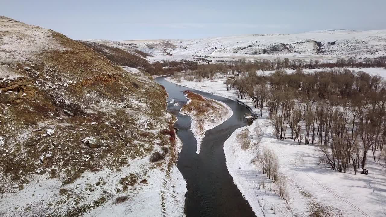 在雪和光秃秃的树木之间的河流航拍，无人机在自然景观上向前上升，对着天空——蒙大拿比林斯视频素材