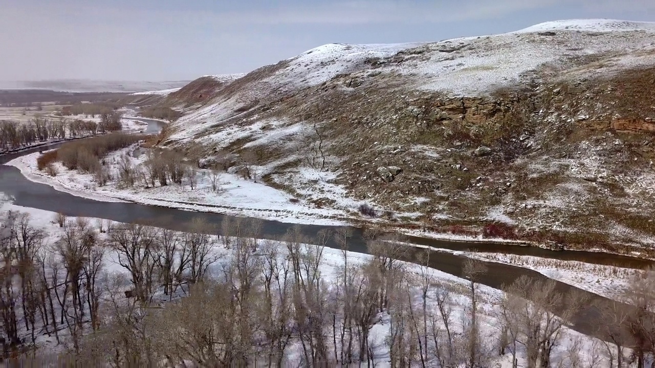 空中平移拍摄的河在光秃秃的树附近的山，无人机飞越雪景-比林斯，蒙大拿州视频素材