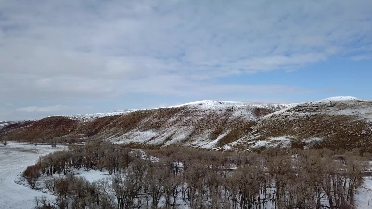 航空拍摄的光秃秃的树木在森林附近的河流和山脉，无人机向前飞行在自然景观对天空-比林斯，蒙大拿州视频素材