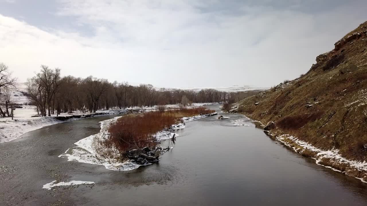 空中拍摄的河在雪和光秃秃的树对着天空，无人机向前飞行在自然景观-比林斯，蒙大拿州视频素材