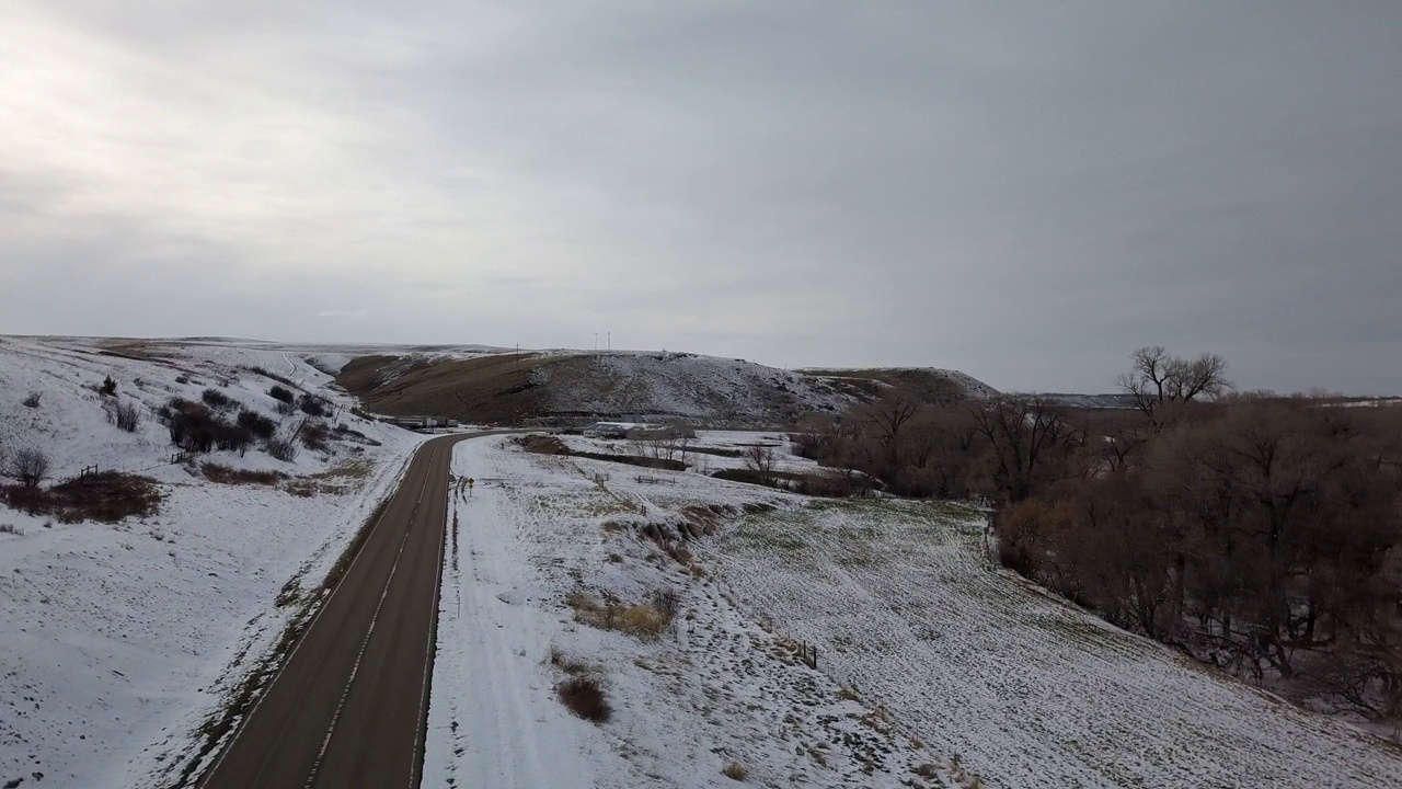 无人机在蒙大拿比林斯的自然景观上飞行，空无一人的道路在雪中，光秃秃的树木映衬着天空视频素材