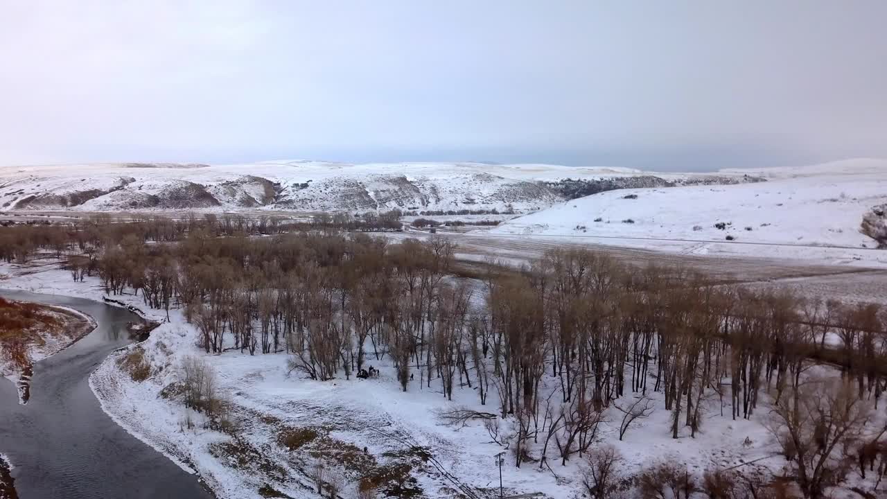 航空拍摄的光秃秃的树木附近的河流附近的雪山，无人机上升在森林在冬季-比林斯，蒙大拿州视频素材