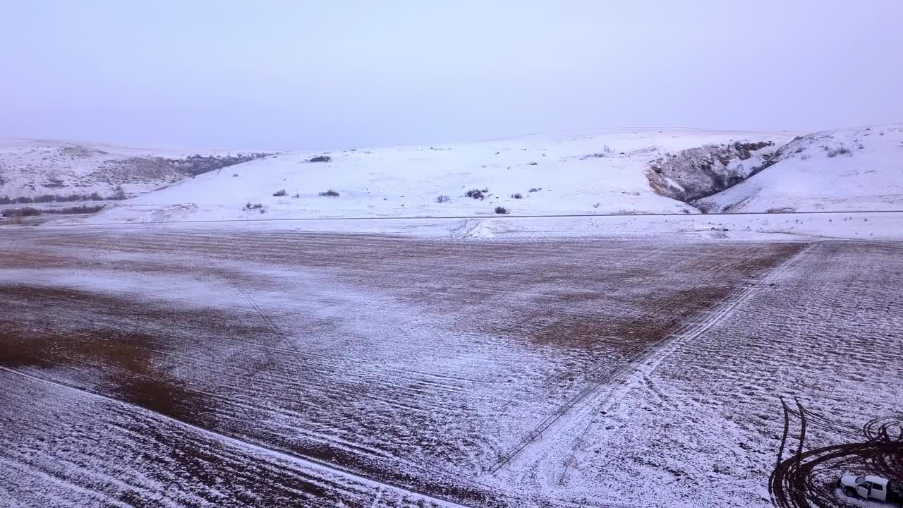 在蒙大拿比林斯，光秃秃的树木和山脉附近的雪地上的车辆的航拍镜头，日落时无人机在森林上空对着天空飞行视频素材