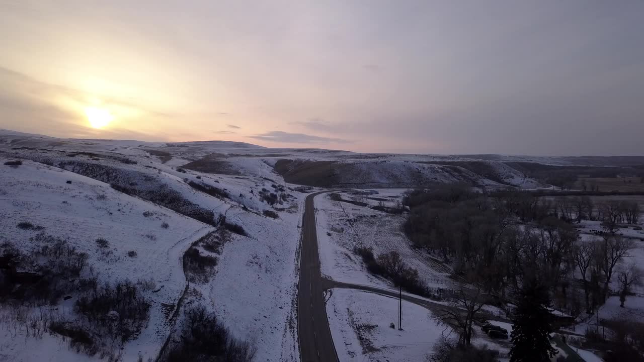 空中拍摄的空旷的道路附近光秃秃的树木和山脉，无人机在日落时向后飞越雪景对天空-比林斯，蒙大拿州视频素材