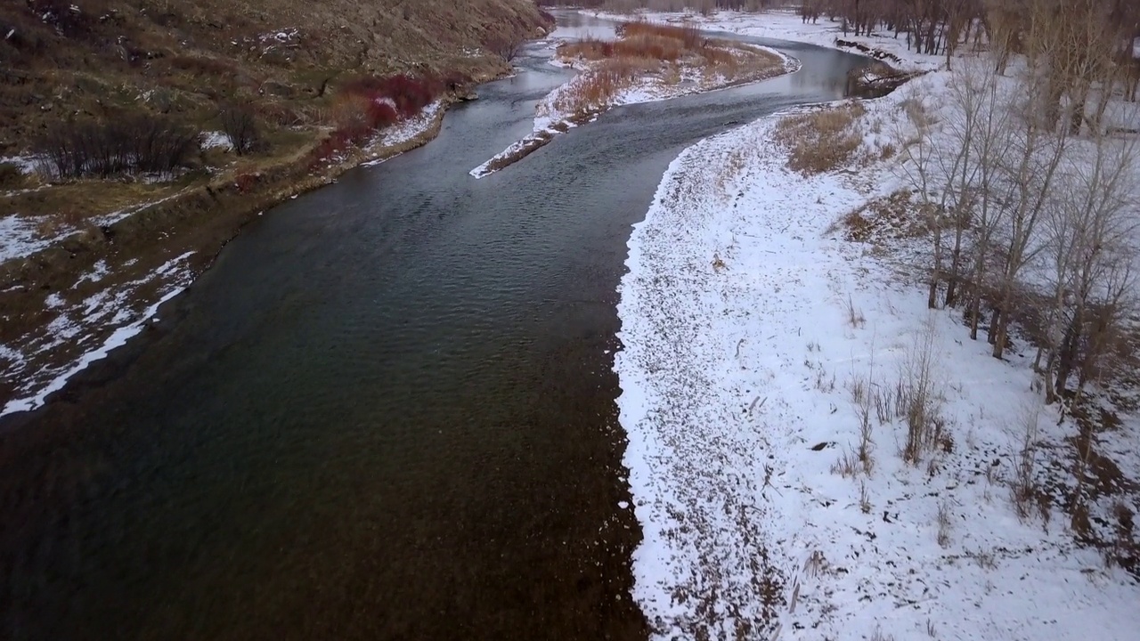 空中倾斜拍摄的河流被雪在森林和山区，无人机向前飞行在自然景观对天空-比林斯，蒙大拿州视频素材