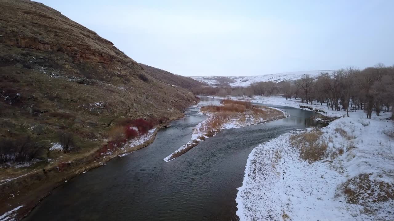 空中拍摄的河流在森林和山脉的雪对着天空，无人机向前飞行在自然景观-比林斯，蒙大拿州视频素材