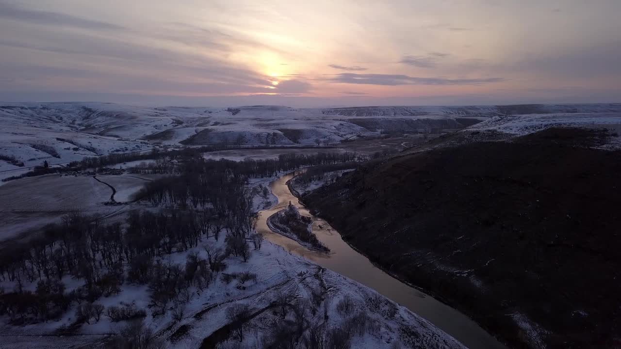 空中拍摄的光秃秃的树木靠近河流和白雪皑皑的山脉，在日落时，无人机在森林上空对着天空飞行——蒙大拿州比林斯视频素材