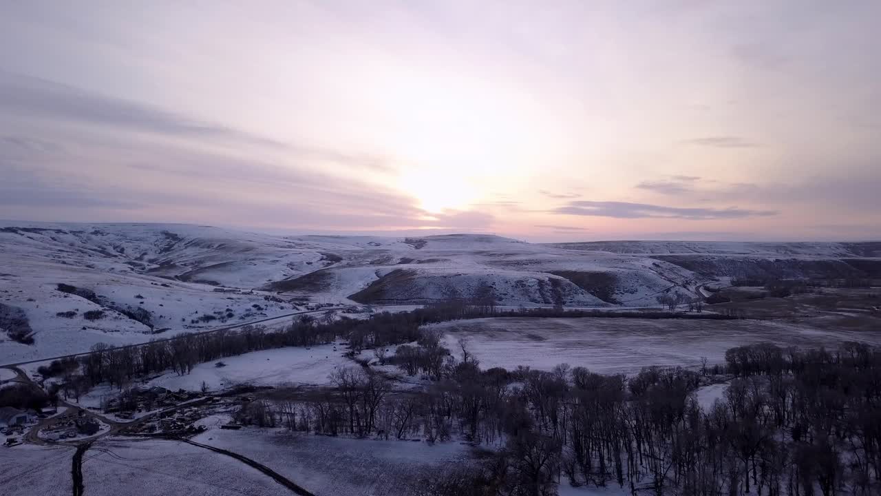 空中平移拍摄的光秃秃的树木附近的河流和雪山，无人机飞越森林对天空在日落-比林斯，蒙大拿州视频素材