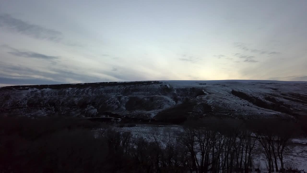 空中拍摄的剪影光秃秃的树木附近的白雪皑皑的山脉，无人机向前飞行在森林对天空-比林斯，蒙大拿州视频素材