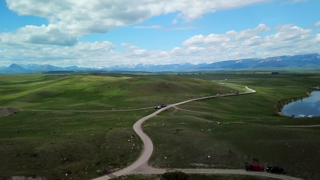 空中拍摄的皮卡车在绿色景观的道路上，无人机下降到植物附近的湖-比林斯，蒙大拿州视频素材