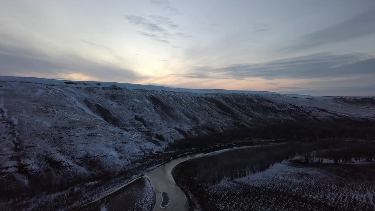 航空拍摄的河附近光秃秃的树和山，无人机下降在雪景对天空在日落-比林斯，蒙大拿州视频素材