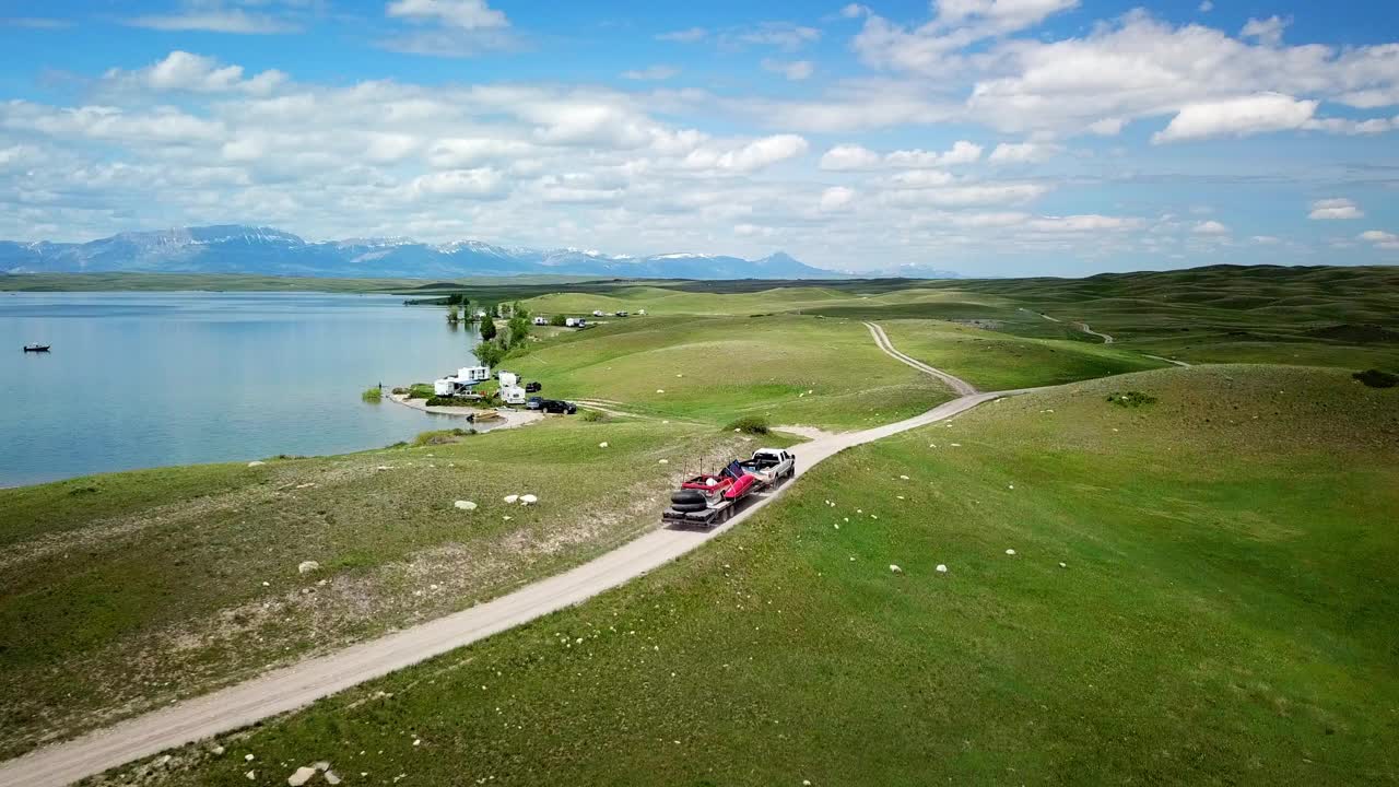 空中拍摄的皮卡车和拖车在湖边的土路上，无人机在多云的天空下飞过绿色景观，蒙大拿比林斯视频素材