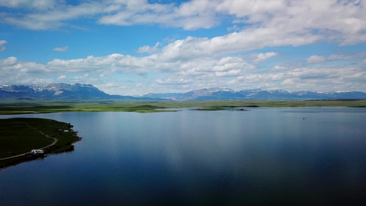 在蒙大拿州比林斯，在多云的天空下，无人机在水面上向后飞行，从空中拍摄的山脉附近的湖泊视频素材