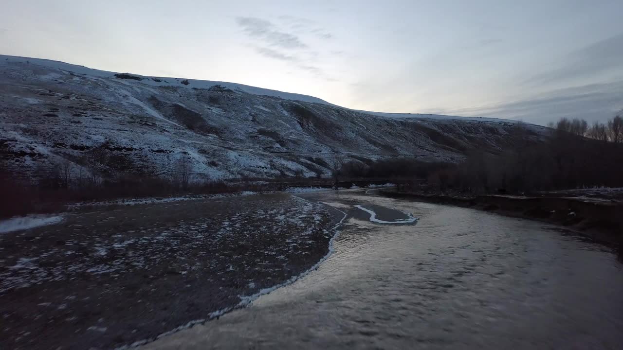 日落时雪山附近的河流航拍，无人机在自然景观上向前上升，对着天空——蒙大拿比林斯视频素材