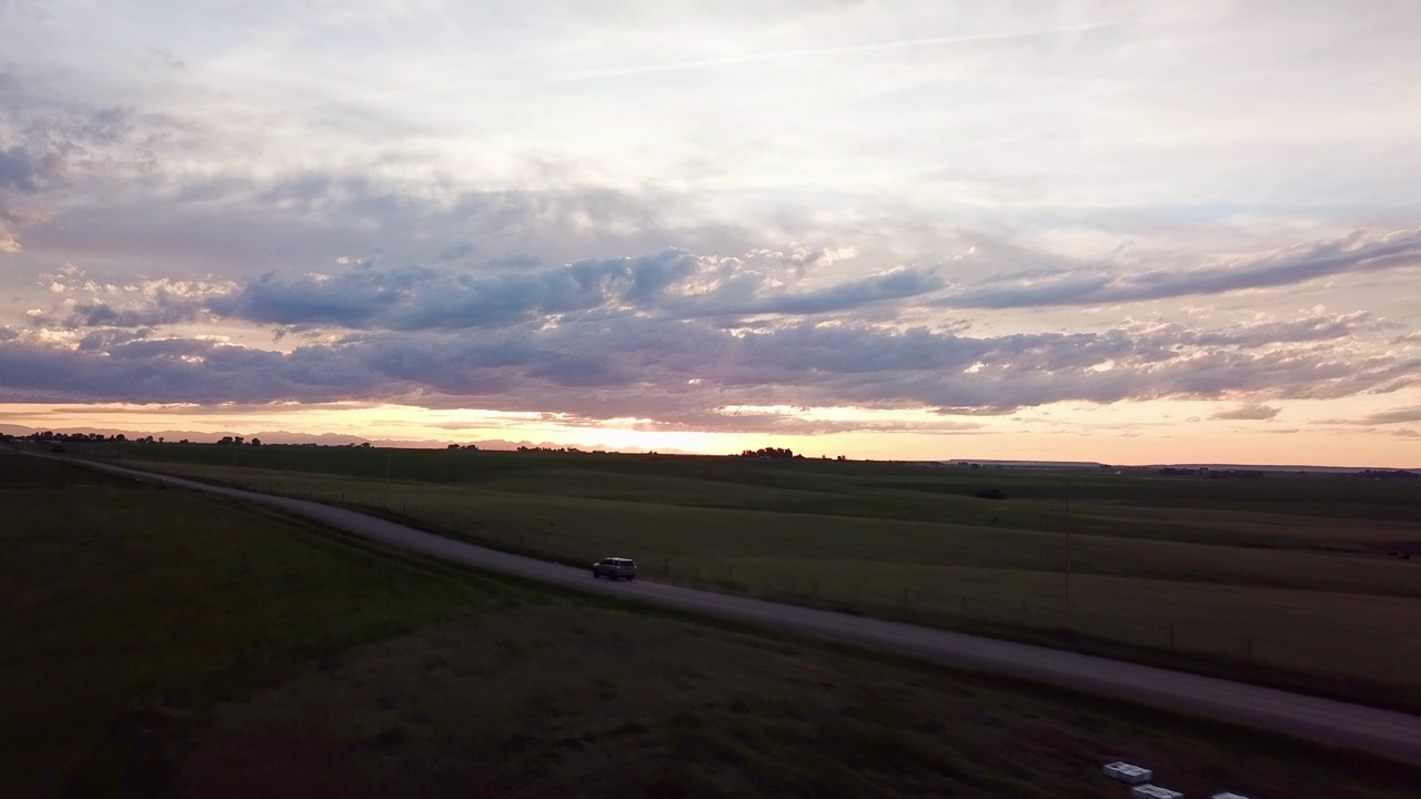 汽车在乡村道路上移动的航拍，在夕阳的天空，无人机飞过风景优美的景观-比林斯，蒙大拿州视频素材