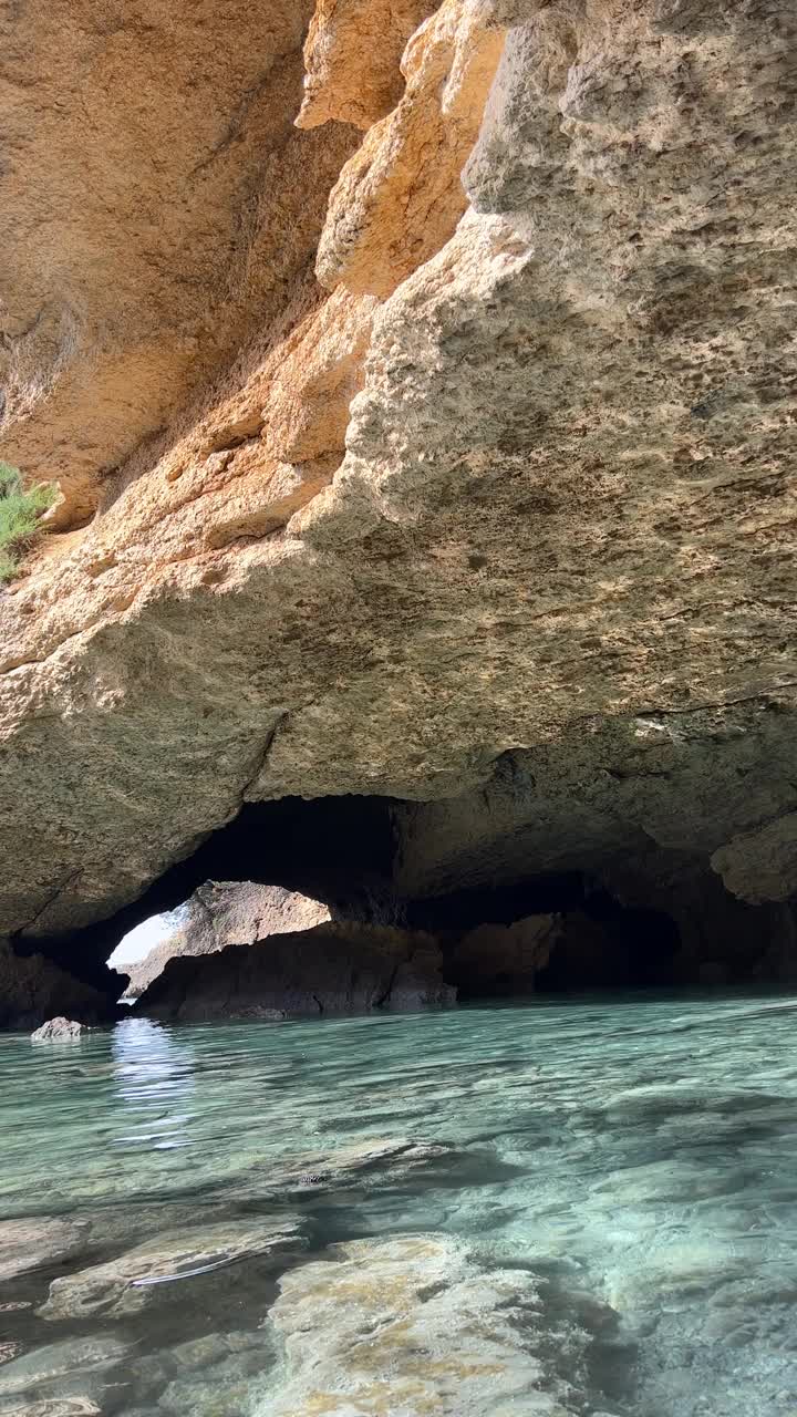 海洞石窟有闪亮的光反射在岩石表面和清澈的蓝色水，垂直视频。视频素材