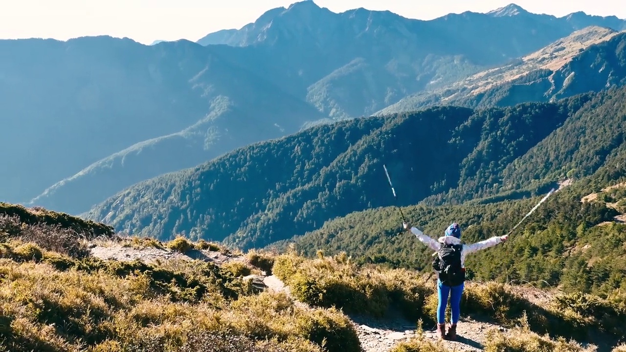 在山顶上高举双臂的徒步旅行者背对着群山。视频素材