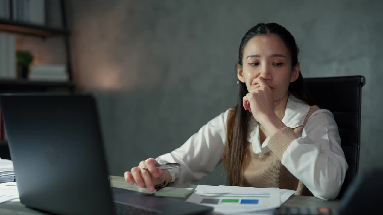 加班期间，一位亚洲年轻成年女性正坐在办公桌前计算要在截止日期前完成的项目预算。视频素材