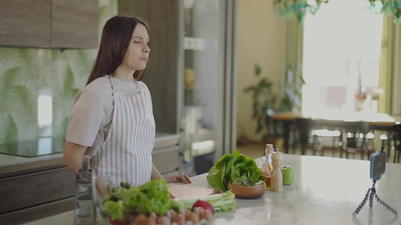 快乐的博主女孩谈论健康的生活方式和拍摄视频食谱。她手里拿着苹果和西红柿。女孩对着智能手机摄像头看了看并说话。慢动作视频素材