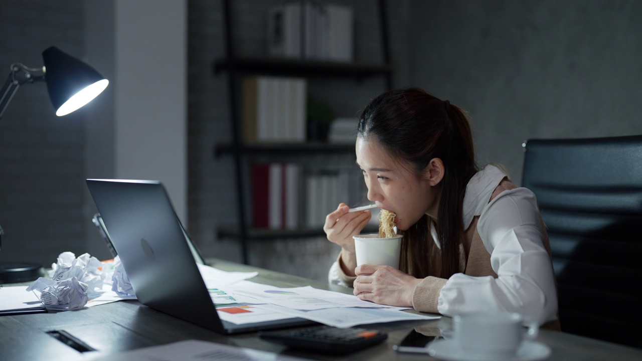 图为，一名亚洲年轻女子正在加班工作，一边吃着速溶杯面。视频素材