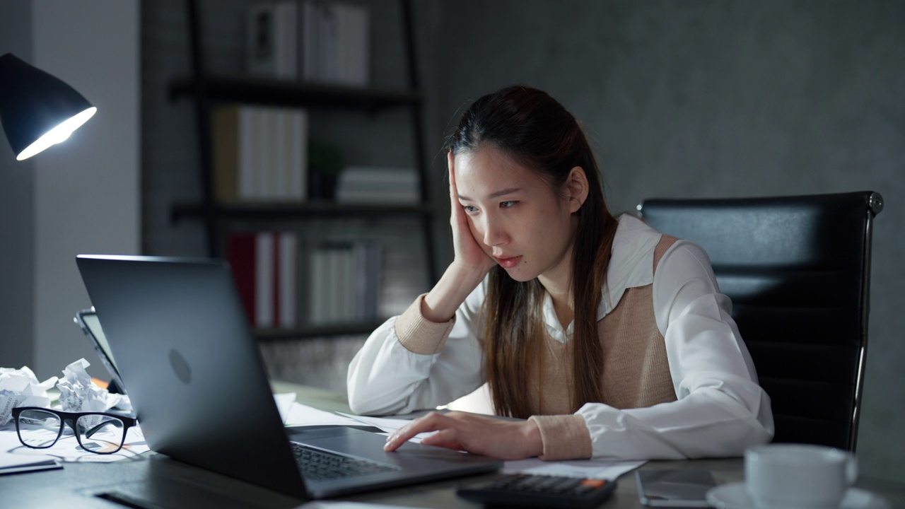 一位亚洲年轻的成年女性在加班期间，正在办公桌前做一个项目计划，以便在截止日期前完成。视频素材