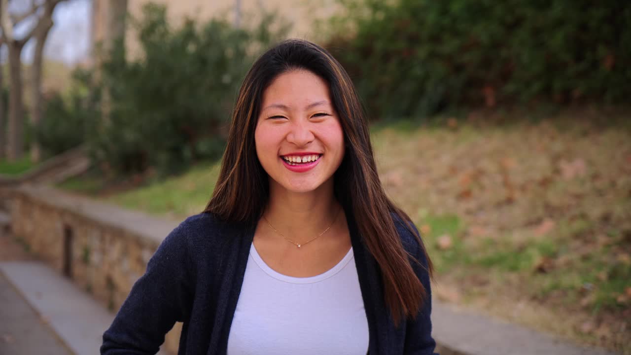 中国年轻女子的近距离个人肖像，微笑着看着外面的相机。正面的亚洲少女笑与友好的态度。乐观的女士，有着洁白的牙齿视频素材