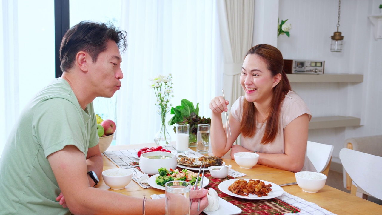 幸福的亚洲家庭，丈夫和妻子在家里的厨房里一起吃晚餐，幸福的夫妇一起吃午餐，约会和蜜月，生活方式和营养理念。视频素材