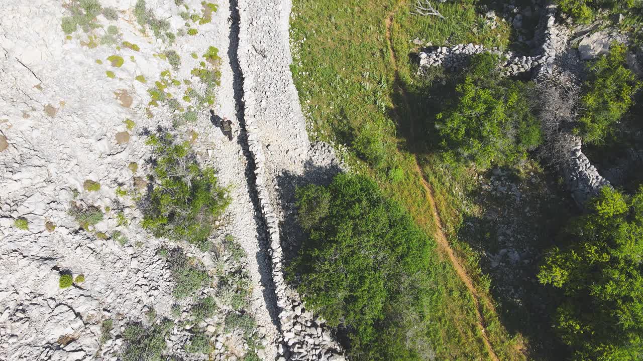 无人机拍摄的徒步旅行者在一条被常绿森林环绕的白色岩石小道上视频下载