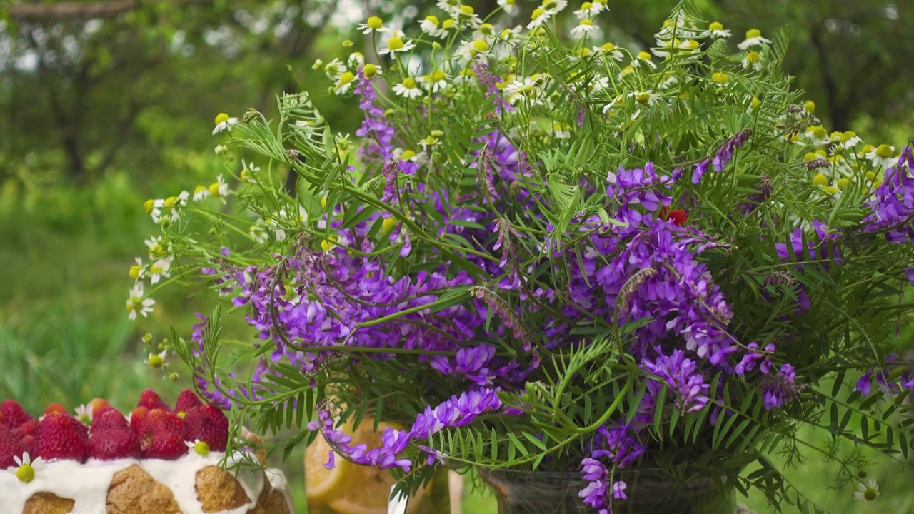 夏日草莓蛋糕、花束、柠檬水和玻璃杯在夕阳的照耀下映照在花园里视频素材