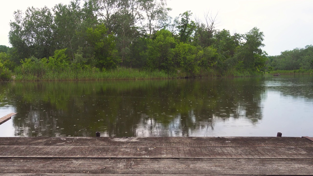 夏日的雨洒在宁静的河上，前景是木码头视频素材