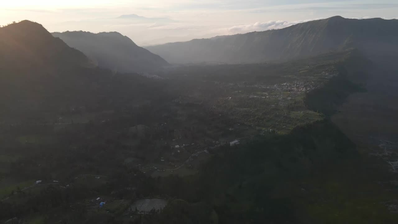 鸟瞰图:夕阳下的印度尼西亚，绿色的山丘上有乡村房屋和山脉视频素材