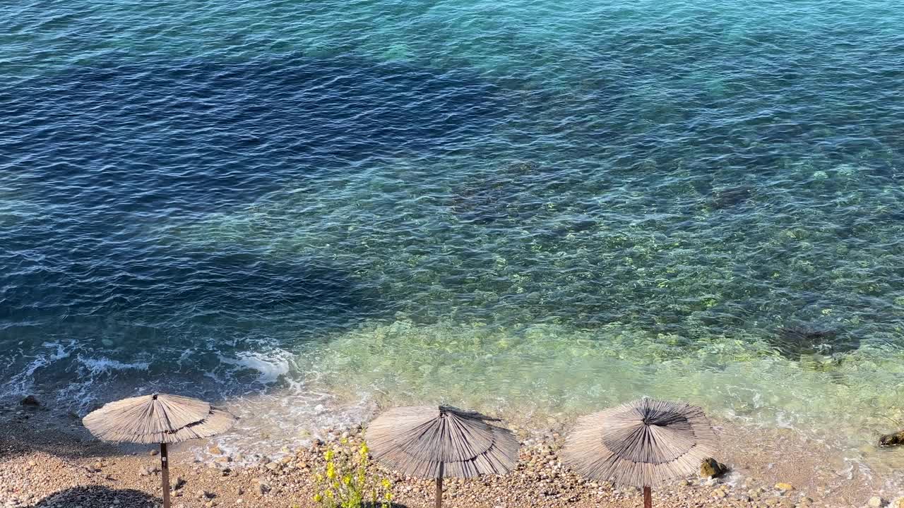 海浪和沙滩上的草编遮阳伞。视频素材