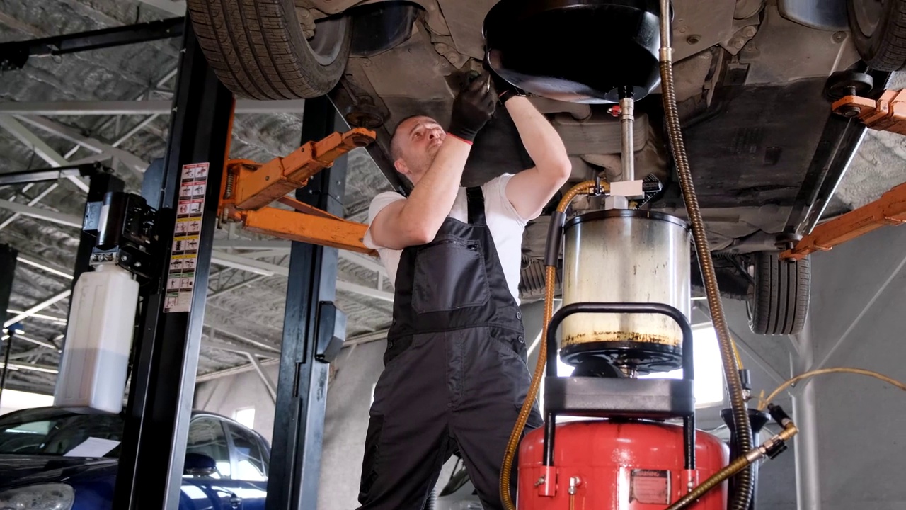 A worker working under a car changes the engine oil. A car mechanic works at a car service视频素材