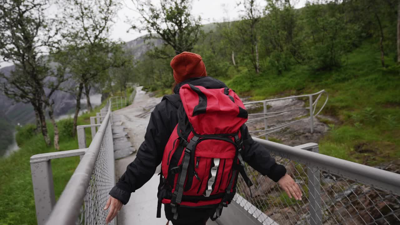 后视图，背着红色大背包的旅行者沿着挪威著名的沃林福森瀑布散步视频素材