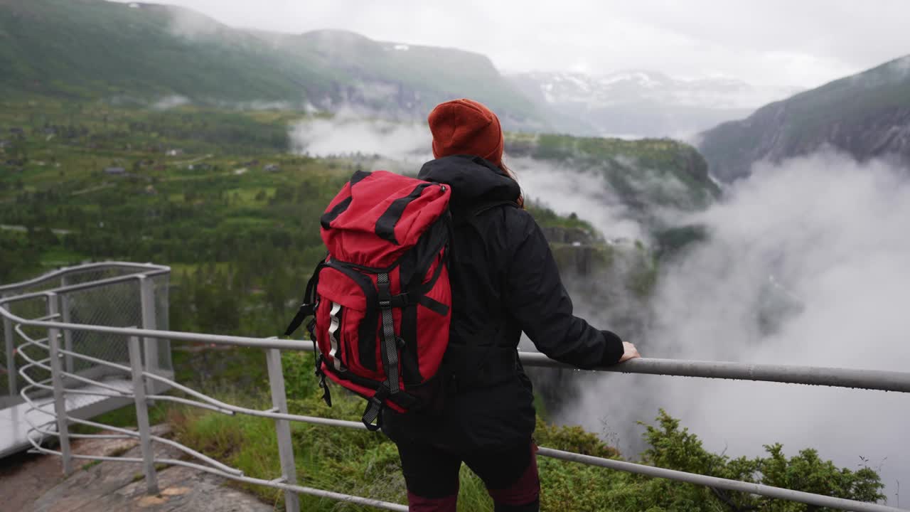 后视图，背着红色大背包的旅行者沿着挪威著名的沃林福森瀑布散步视频素材