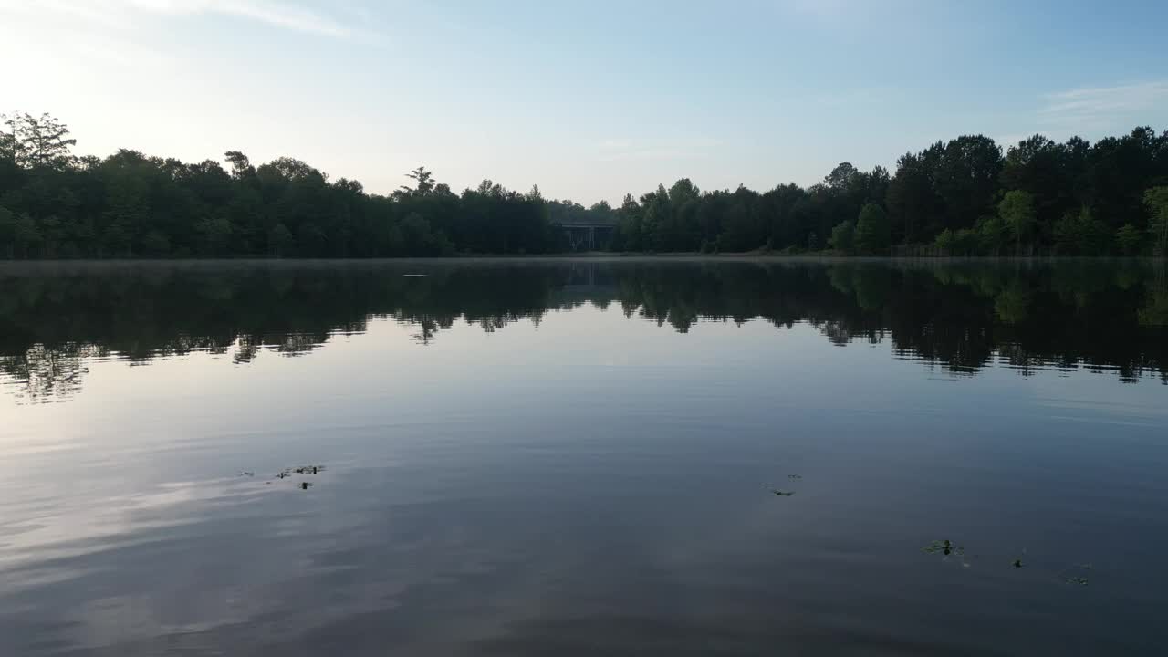 夕阳下，无人机在湖面上拍摄树木和桥梁的倒影视频素材