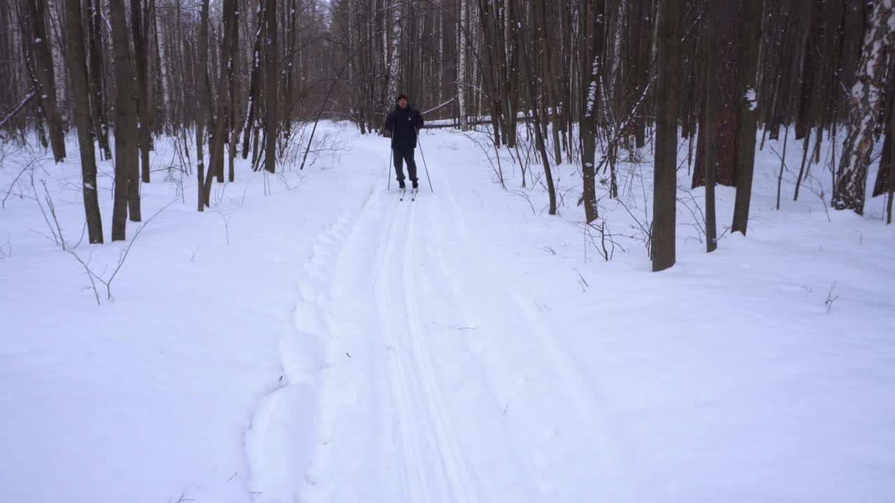 一个50岁的男人冬天在森林里滑雪视频素材