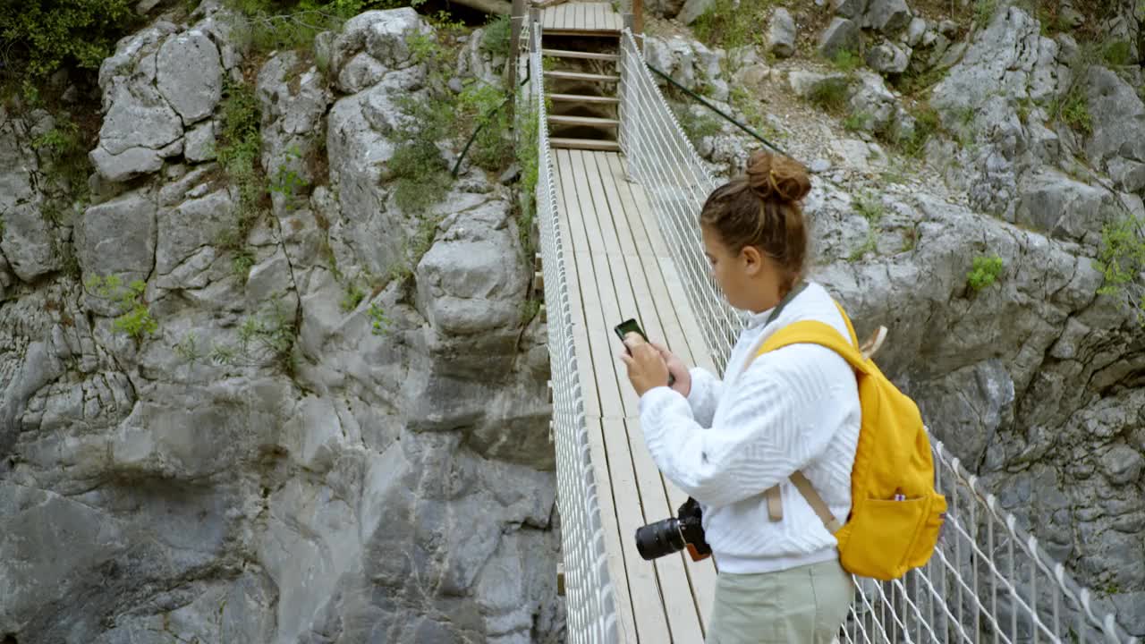 年轻女子徒步旅行者在穿越山涧悬索桥时使用手机地图。视频素材