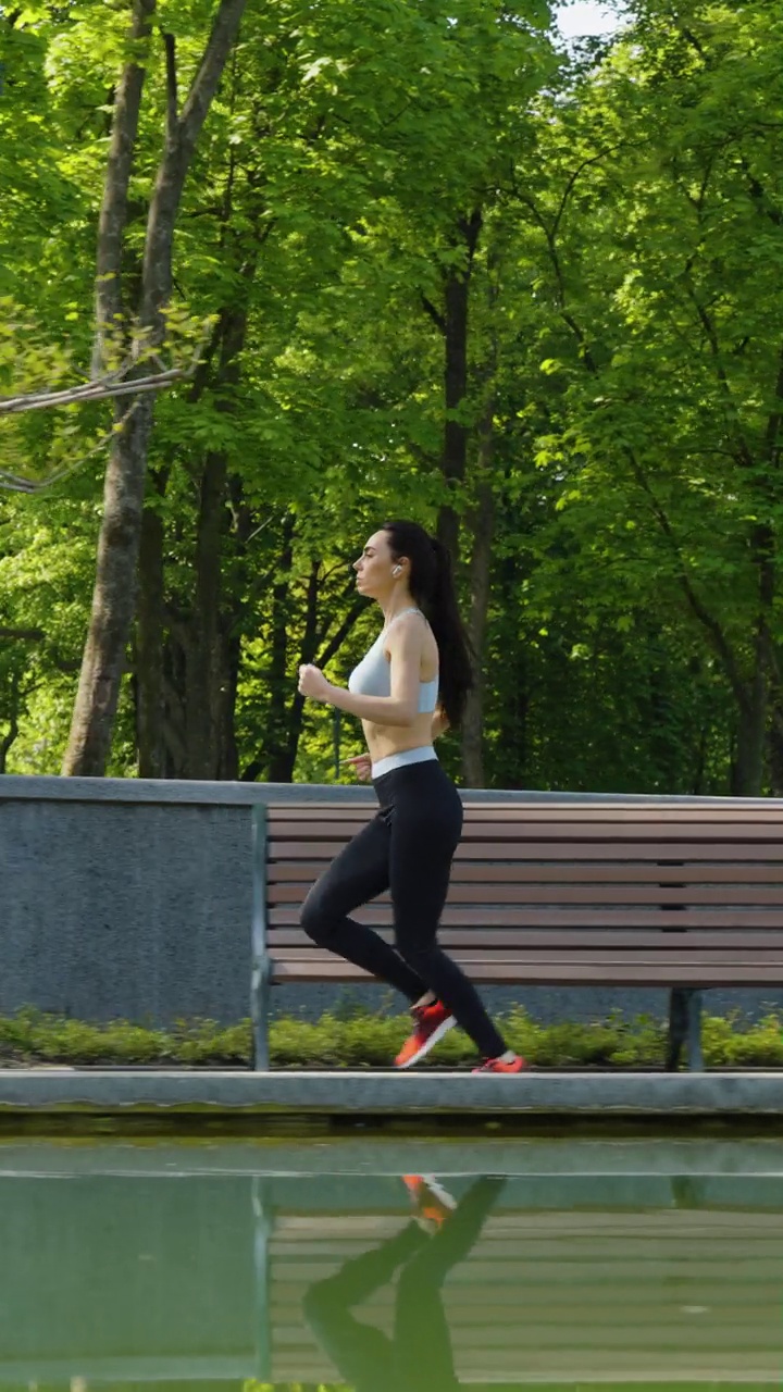 竖屏:健美女子在公园池塘边慢跑视频素材