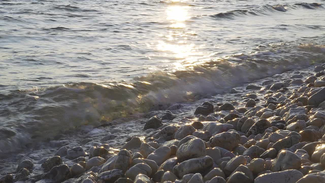 日落时分，海浪冲击着卵石滩的海岸视频下载