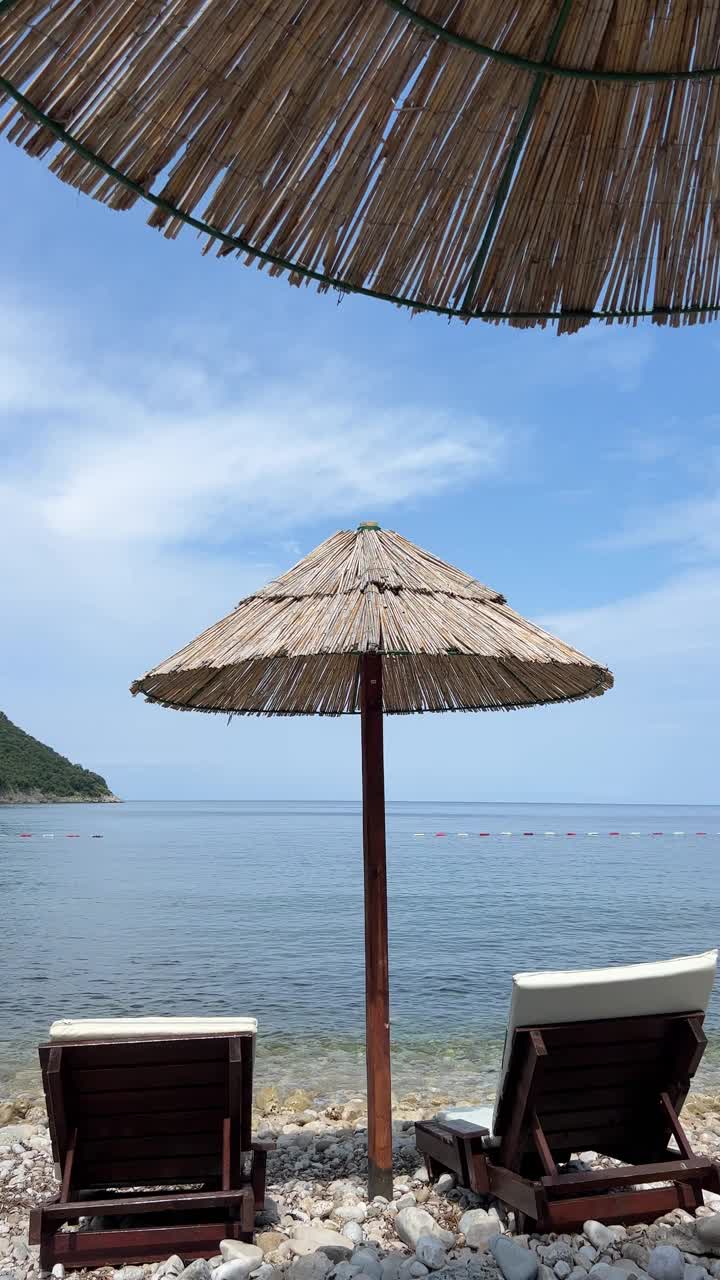 海水湛蓝，卵石沙滩，夏天有遮阳伞和日光浴床。视频素材