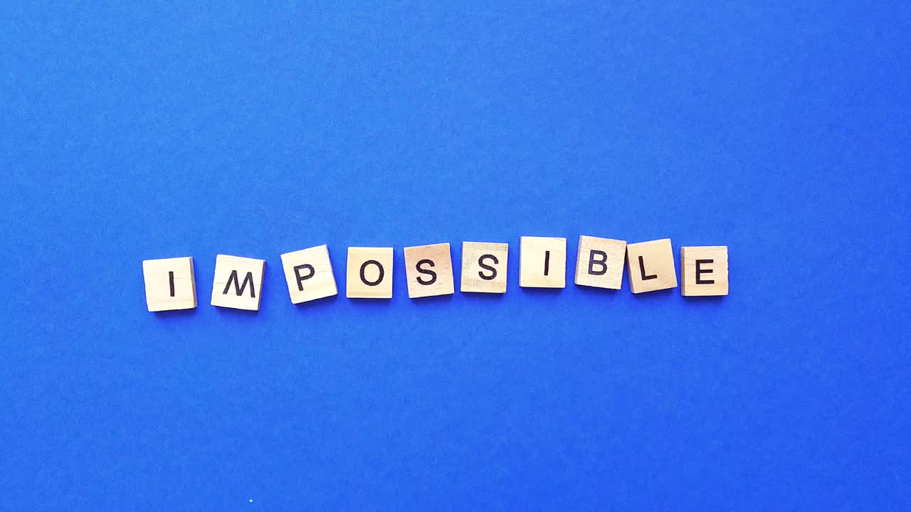 通过在蓝色背景上手动移除立方体，将单词impossible从木制字母变为possible。俯视图视频下载