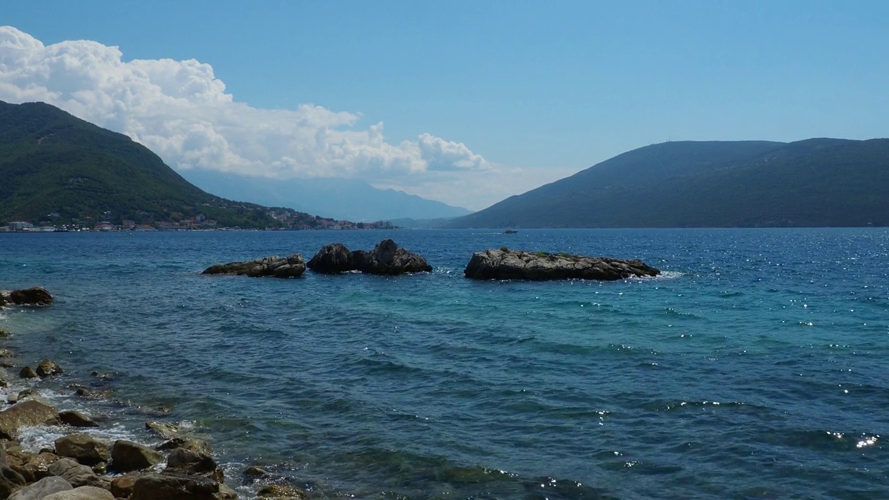 黑山Herceg Novi。海边度假。海上旅行。小船漂浮在亚得里亚海上。地中海旅游业务。山脉。水面上的小涟漪。天空在波浪中的反射。Boka-Kotor海滩视频素材