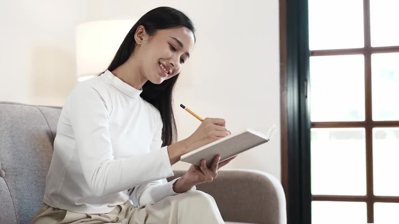 积极放松的女孩学习她的笔记。年轻的亚洲女子坐在马车上看她的笔记本。在家学习的概念视频素材