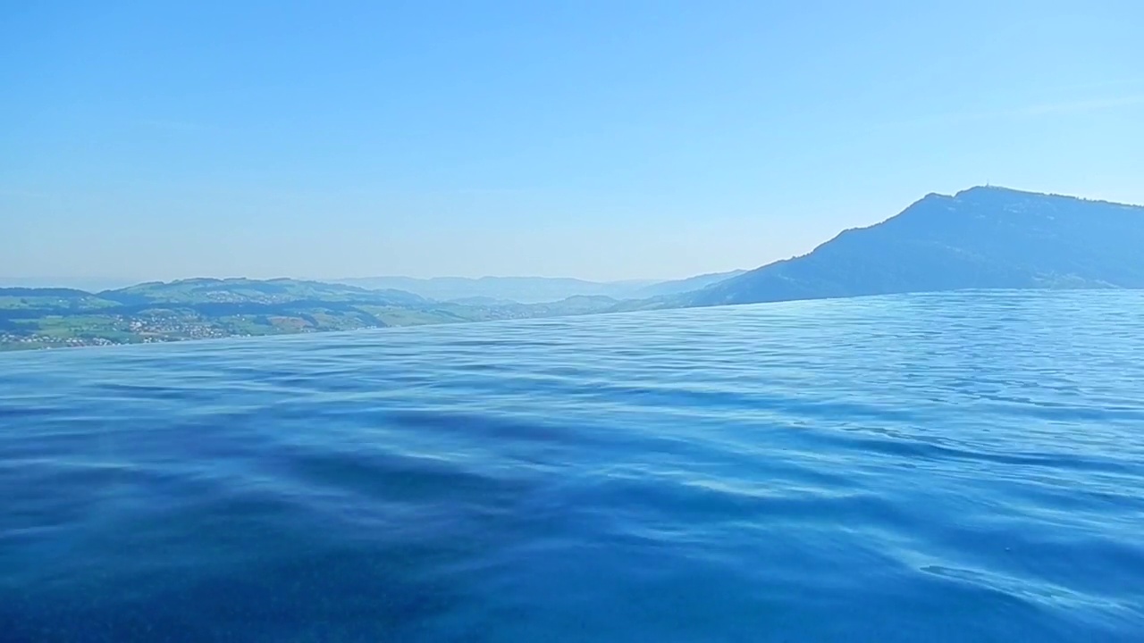 在一个阳光明媚的夏日，在卢塞恩湖上，拥有山景和湖景的无限游泳池视频素材