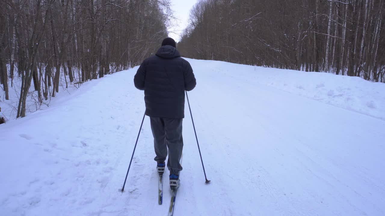 一个50岁的男人冬天在森林里滑雪视频素材