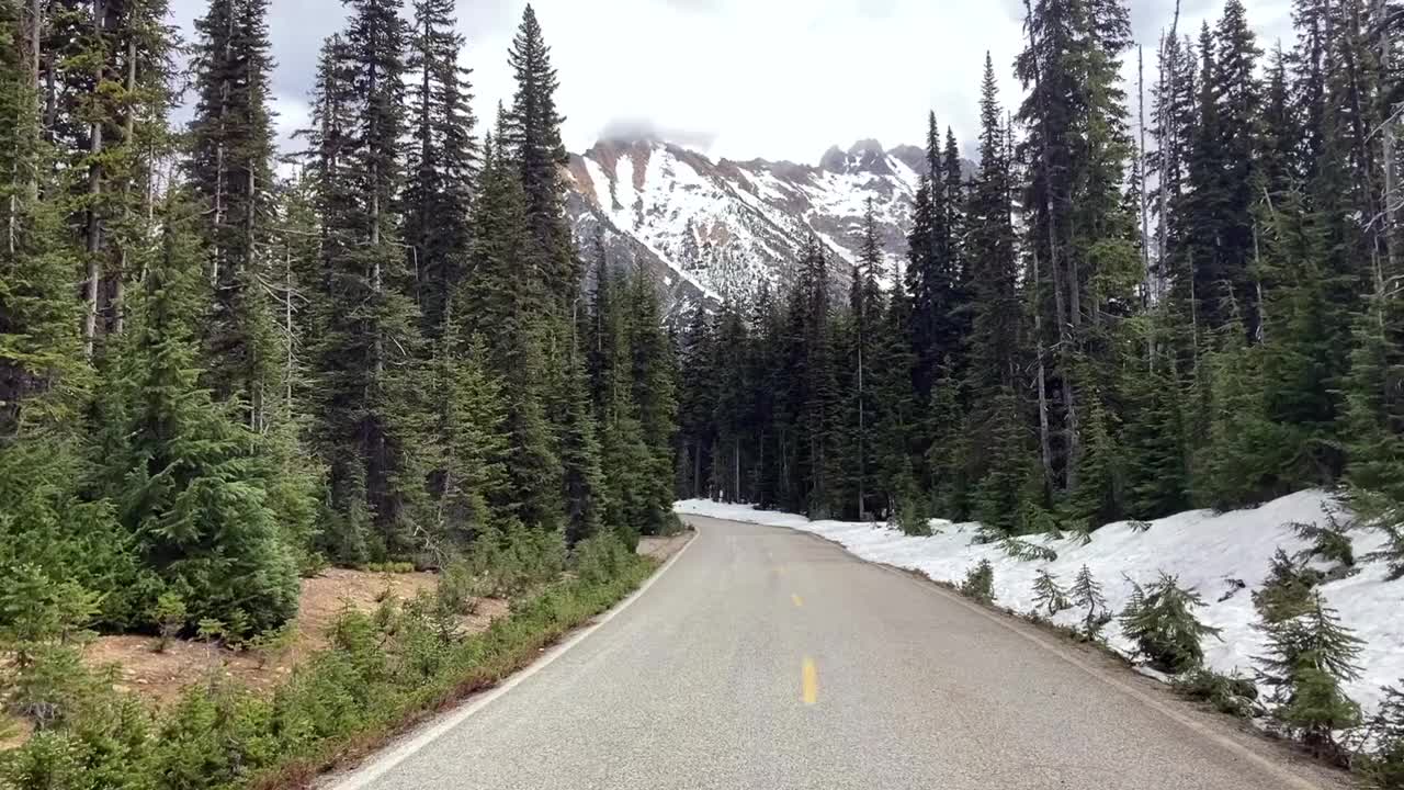 沿着空旷的乡村道路，看到白雪皑皑的山脉和常绿的树木视频素材