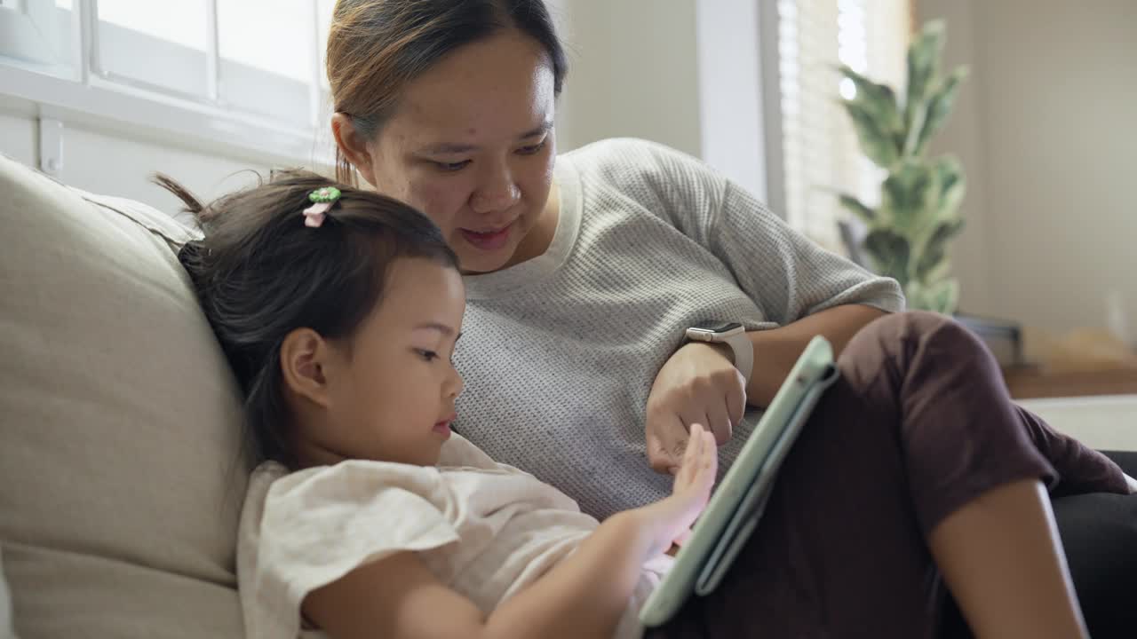 母女俩喜欢在家里一起使用数字平板电脑放松视频素材